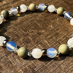 Pode incluir: Um bracelete feito com contas azuis claras, brancas e marrons. As contas são enfiadas em uma corrente prateada.