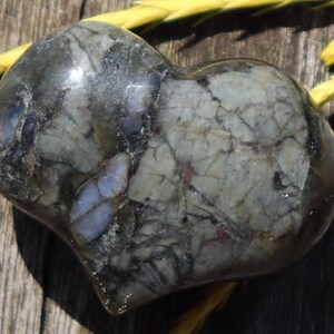 May include: A heart-shaped stone with a dark grey, green, and white marbled pattern. The stone has a smooth, polished surface.