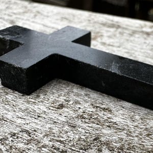May include: A white ceramic mug with a black handle and the text "But First, Coffee" in a bold, black font. The mug is set against a blurred background, suggesting a cozy setting.