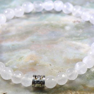 May include: White gemstone bracelet with a silver charm. The bracelet is made of round beads and has a simple design.