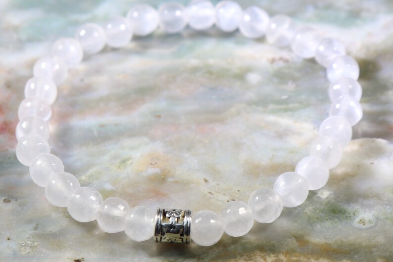 May include: White gemstone bracelet with a silver charm. The bracelet is made of round beads and has a simple design.