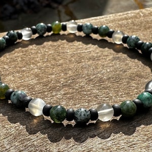 May include: A green, black, and white beaded bracelet with a variety of stones.