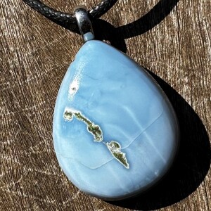 May include: A teardrop-shaped pendant necklace with a light blue stone featuring a white and green pattern. The pendant is attached to a black cord.