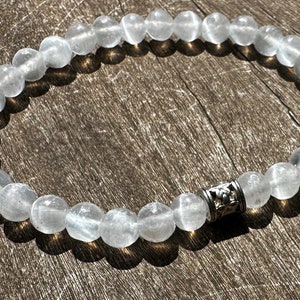 May include: A white gemstone bracelet with a silver charm. The bracelet is made of round beads and has a simple design.