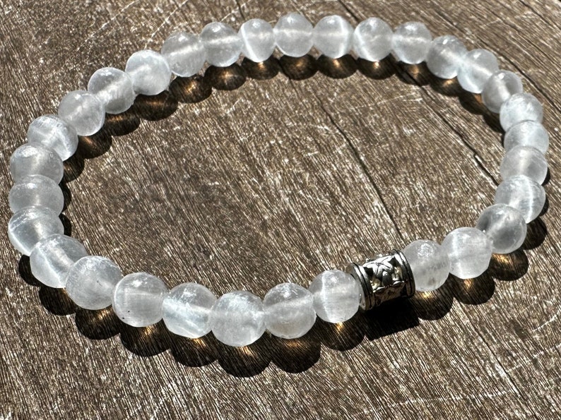 May include: A white gemstone bracelet with a silver charm. The bracelet is made of round beads and has a simple design.