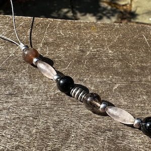 May include: A beaded phone charm with a brown, pink, black, and clear crystal beads. The beads are strung on a silver cord.