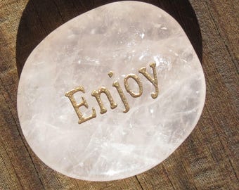 Peut inclure: Une pierre lisse, blanche et en forme de cœur avec le mot "Enjoy" inscrit en lettres dorées.