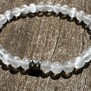 May include: A white gemstone bracelet with a silver bead charm. The bracelet is made of round, smooth beads and is approximately 7 inches in length.