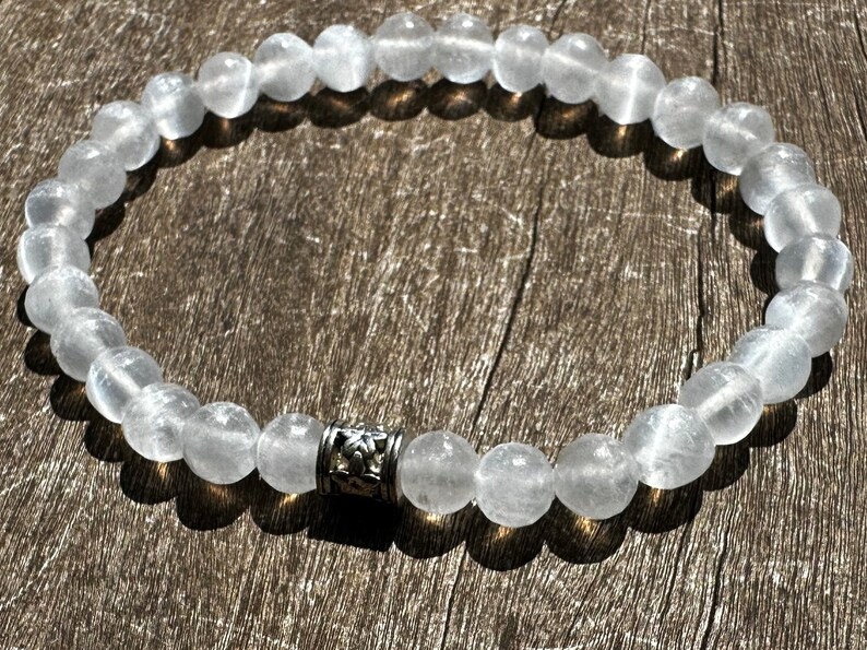 May include: A white gemstone bracelet with a silver bead charm. The bracelet is made of round, smooth beads and is approximately 7 inches in length.