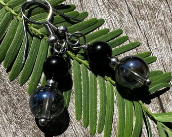 May include: Black and silver beaded earrings with a silver hook closure. The beads are round and have a shiny finish.