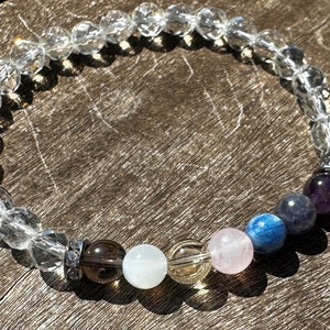 Può includere: Un braccialetto di cristallo con perline di quarzo trasparente e una varietà di pietre colorate, tra cui ametista, cianite blu, pietra di luna e quarzo rosa.