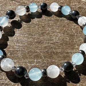 May include: A bracelet made with alternating beads of white, light blue, and black. The bracelet is made with natural stones.