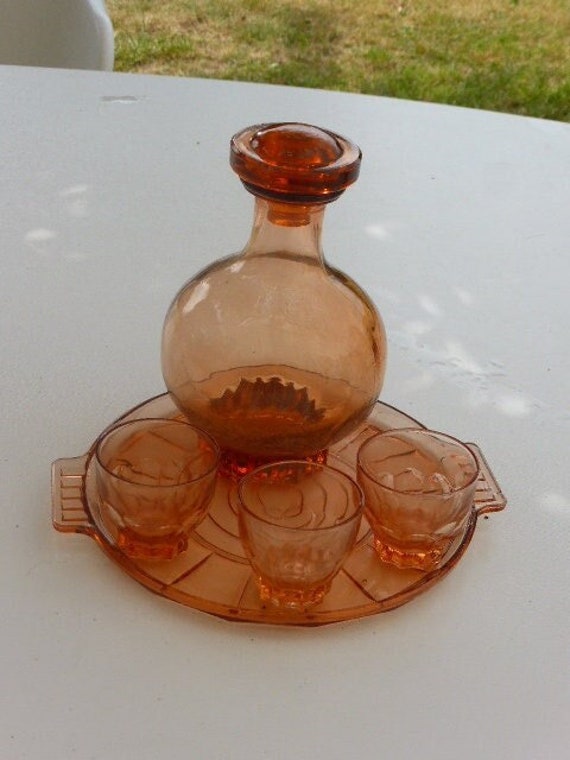 Liquor service in coral pink glass, consisting of a round tray, a bottle decanter and three small vintage glasses 1940