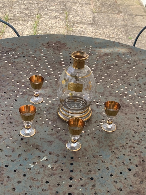 Liqueur set, consisting of a bottle with a gold and white floral motif and four small gold glasses, by CADOVERRE France, vintage,