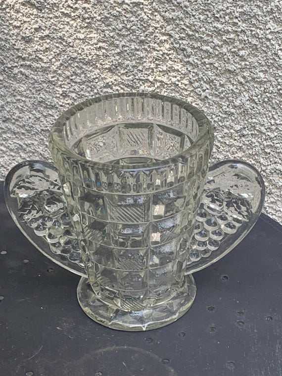 Clear glass angel wings vase with raised geometric patterns, handles with bunches of grapes