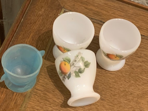 Set of 4 egg cups, 3 in arcopal glass with fruit pattern and one in blue plastic in the shape of a hen