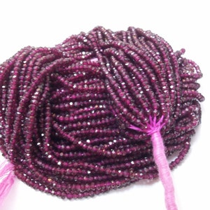 May include: A strand of deep red faceted gemstone beads. The beads are small and uniform in size, and they are strung on a thin thread. The beads are arranged in a loose, flowing pattern, and they have a subtle sparkle.