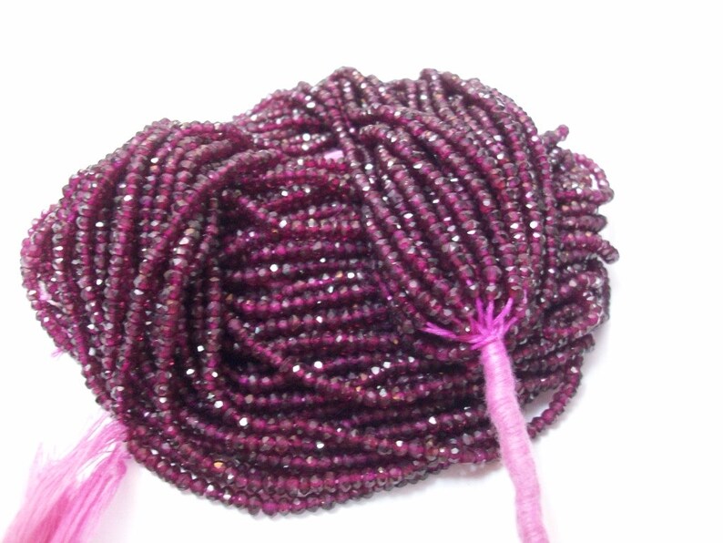 May include: A strand of deep red faceted gemstone beads. The beads are small and uniform in size, and they are strung on a thin thread. The beads are arranged in a loose, flowing pattern, and they have a subtle sparkle.
