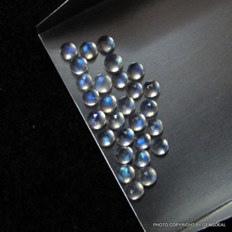 Puede incluir: Una colecci&oacute;n de 25 cabujones redondos de piedra lunar iridiscente. Las piedras son de color blanco p&aacute;lido con un brillo azul.