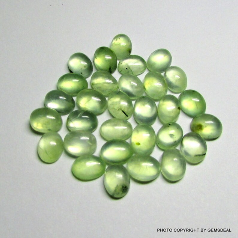 May include: A collection of 30 oval-shaped green gemstones. The stones are smooth and polished, with a translucent appearance.
