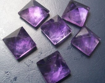 May include: Six purple amethyst crystal pyramids, each with a square base and four triangular sides, arranged on a dark gray surface.