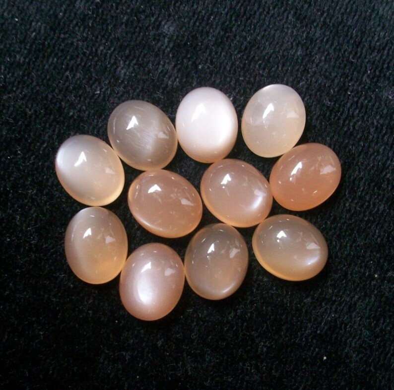 May include: A collection of twelve oval-shaped moonstone cabochons in various shades of white and peach.