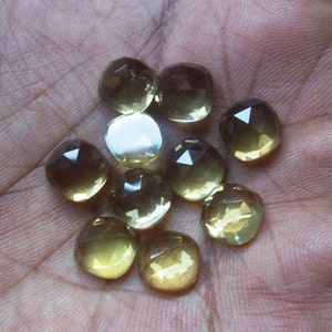 May include: A collection of ten faceted, clear, light yellow gemstones. The gemstones are various sizes and shapes, with some having a more rounded shape and others having a more square shape.