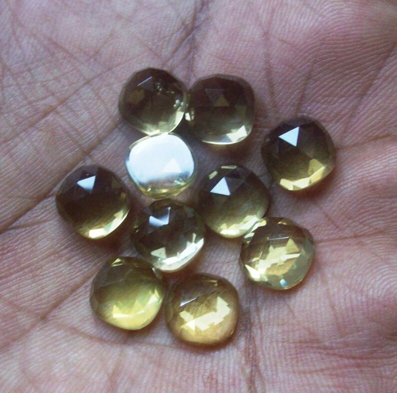 May include: A collection of ten faceted, clear, light yellow gemstones. The gemstones are various sizes and shapes, with some having a more rounded shape and others having a more square shape.