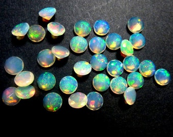 May include: A collection of 25 loose, round, white opal cabochons with iridescent green and blue flashes. The opals are approximately 6mm in diameter.