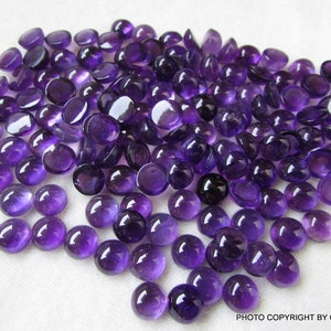 May include: A large group of round, purple amethyst cabochons. The cabochons are smooth and polished, with a slight sheen.