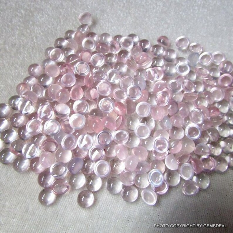 May include: A large pile of round, translucent pink cabochons. The cabochons are smooth and have a slightly cloudy appearance.