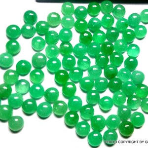 May include: A collection of round, green gemstone cabochons. The cabochons are smooth and polished, with a slightly domed shape. They are arranged in a loose pile, with some overlapping.