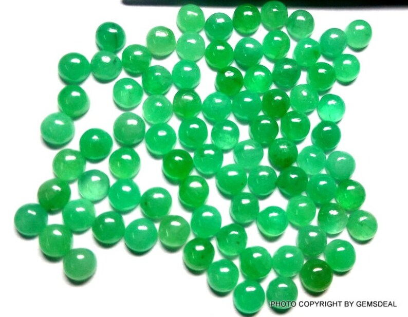 May include: A collection of round, green gemstone cabochons. The cabochons are smooth and polished, with a slightly domed shape. They are arranged in a loose pile, with some overlapping.