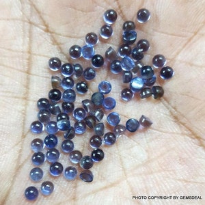 Puede incluir: Una colecci&oacute;n de peque&ntilde;as piedras preciosas redondas azules. Las piedras preciosas son lisas y tienen un ligero brillo. Est&aacute;n esparcidas sobre una mano.