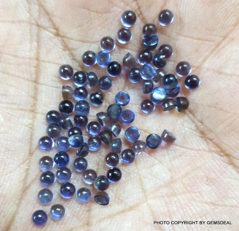 Puede incluir: Una colecci&oacute;n de peque&ntilde;as piedras preciosas redondas azules. Las piedras preciosas son lisas y tienen un ligero brillo. Est&aacute;n esparcidas sobre una mano.