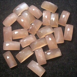 Peut inclure: Une collection de 20 cabochons de pierre de lune rose pâle, chacun de forme rectangulaire et à la surface lisse et polie. Les pierres ont un léger chatoiement et brillance.