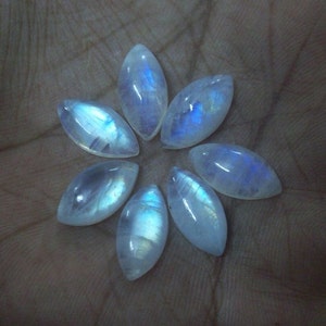 Puede incluir: Siete cabujones de piedra lunar blanca iridiscente en forma de marquesa, dispuestos en forma de flor.