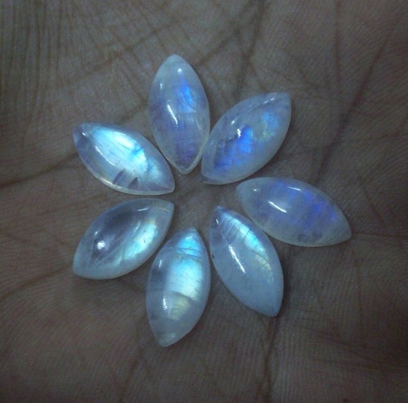 Puede incluir: Siete cabujones de piedra lunar blanca iridiscente en forma de marquesa, dispuestos en forma de flor.
