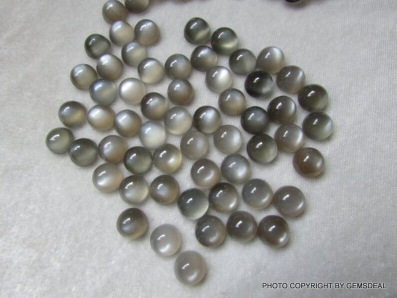 May include: A collection of 50 round, gray moonstone cabochons. The stones are smooth and have a subtle shimmer.