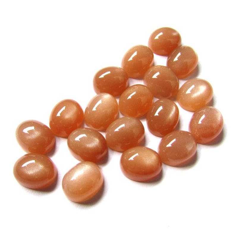 May include: A collection of 18 oval-shaped, peach-colored sunstone cabochons. The stones have a shimmery, iridescent quality.