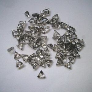 May include: A collection of clear quartz crystal points with black inclusions, also known as rutilated quartz, in a triangular shape. The crystals are scattered on a white surface.