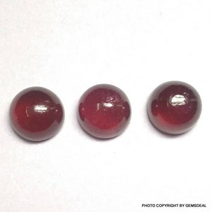 May include: Three round, red gemstones with a smooth, polished finish. The gemstones are arranged in a row on a white surface.