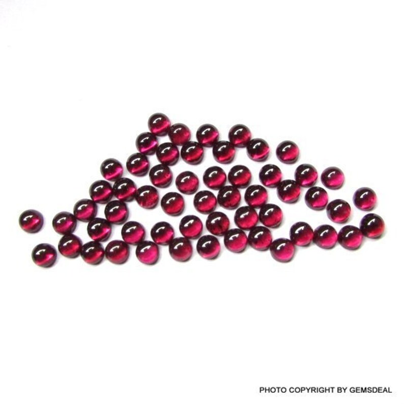May include: A group of 30 round, red gemstone cabochons. The cabochons are smooth and polished, with a slight shine.