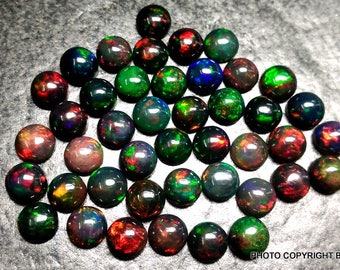 May include: A collection of 30 round black opals with iridescent green, red, and blue flashes. The opals are approximately 6mm in diameter and are displayed on a dark gray surface.