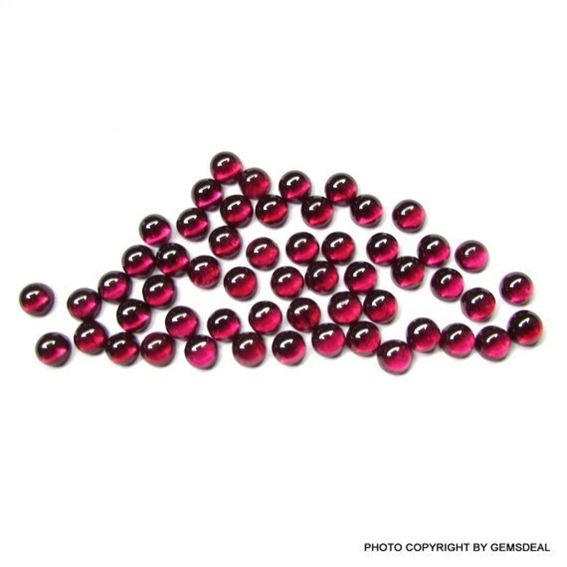 May include: A group of 40 round, red, glass cabochons. The cabochons are scattered on a white surface.
