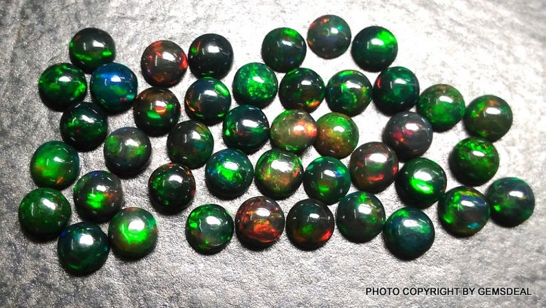 May include: A collection of 30 round, black opal cabochons with green and red flashes. The opals are approximately 6mm in diameter.