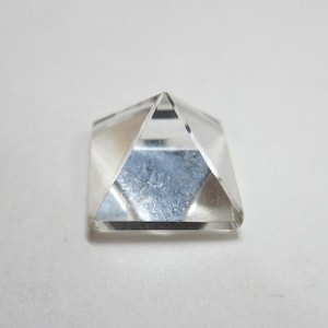 May include: A clear crystal pyramid with a square base. The pyramid is made of polished glass and has a reflective surface.