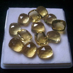 May include: A collection of 12 faceted, yellow gemstones displayed on a white background. The gemstones are various sizes and shapes, with some being more rounded than others.