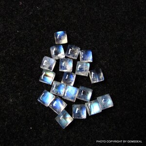 K&ouml;nnte beinhalten: Eine Sammlung von 15 regenbogenfarbenen blauen Mondstein-Quadratcabochons, die jeweils etwa 6 mm x 6 mm messen. Die Steine sind lose und bereit, in Schmuck eingefasst zu werden.