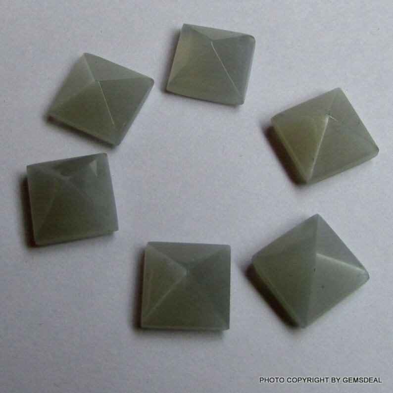 Puede incluir: Seis cabujones de piedra preciosa de forma piramidal gris. Los cabujones son lisos y pulidos.